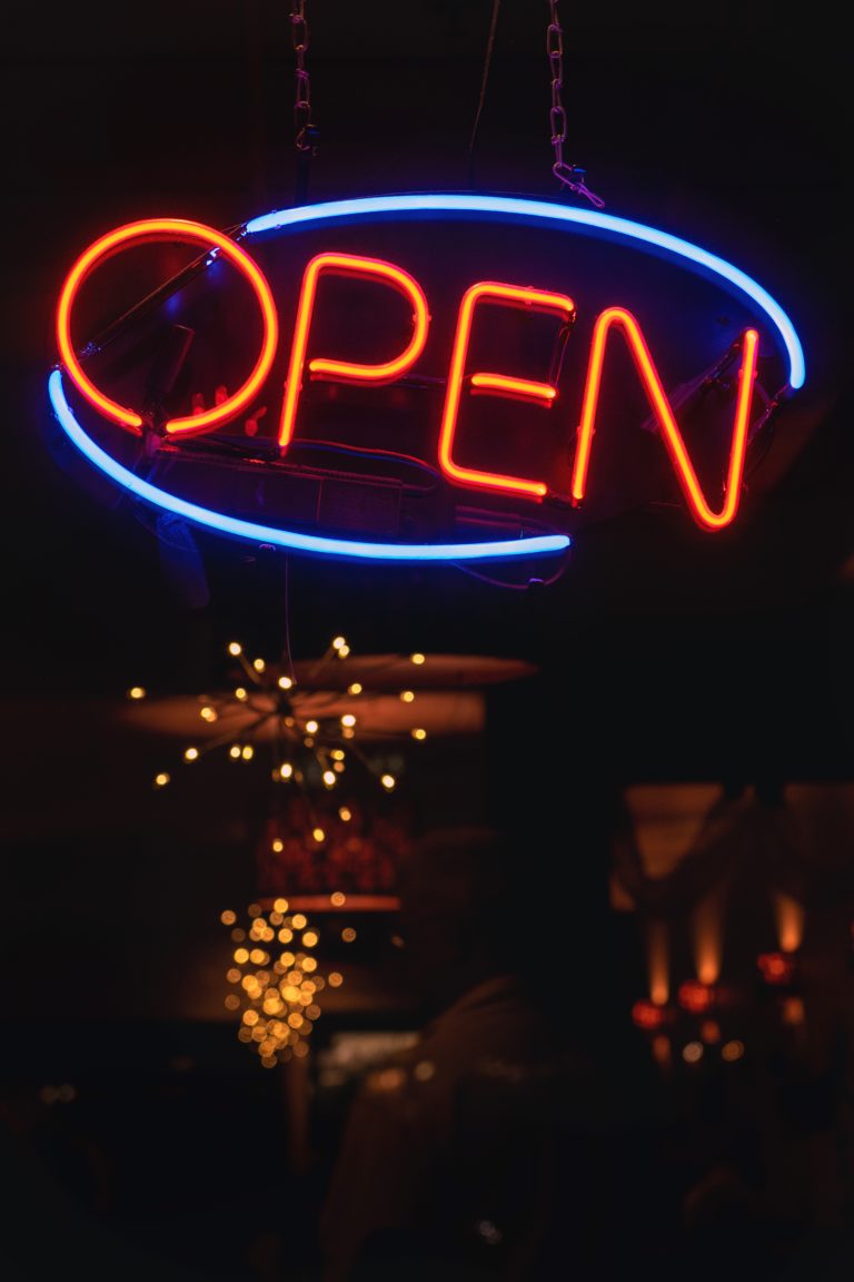A vertical shot of an orange and blue neon sign that says "OPEN" at a bar